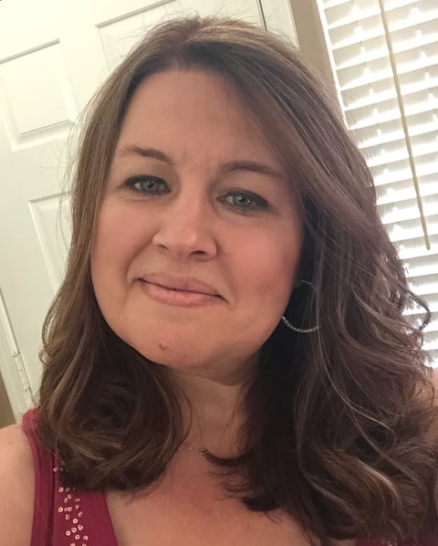 Portrait of a woman with long brown hair and hoop earrings wearing a red sleeveless top, smiling indoors